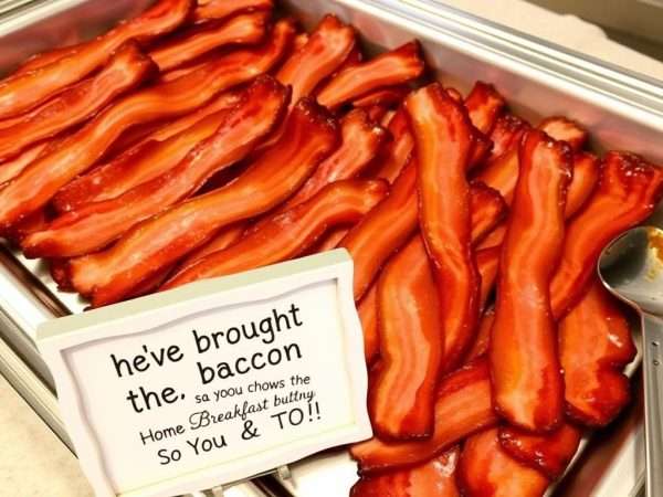 Crispy bacon on a breakfast buffet with a sign featuring a bacon pun about 'bringing home the bacon' Crispy bacon on a breakfast buffet with a sign featuring a bacon pun about 'bringing home the bacon'