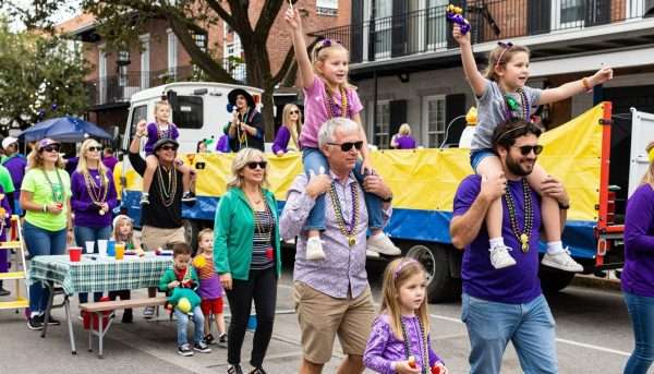Families celebrating Mardi Gras together along St. Charles Avenue with children on shoulders catching throws Families celebrating Mardi Gras together along St. Charles Avenue with children on shoulders catching throws