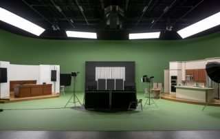 The image captures a bustling modern film studio in Atlanta, Georgia, featuring a sleek green screen and black box soundstage.