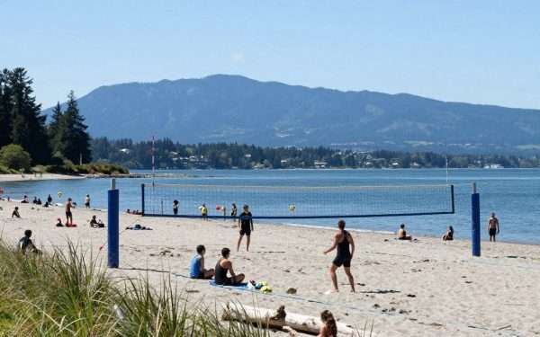 Kitsilano Beach with people playing volleyball, mountains in background Kitsilano Beach with people playing volleyball, mountains in background